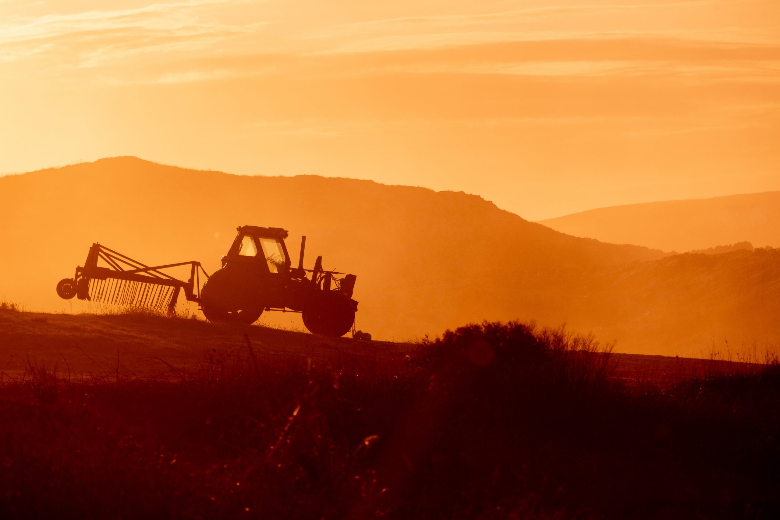 tractor in a farm field at sunset.