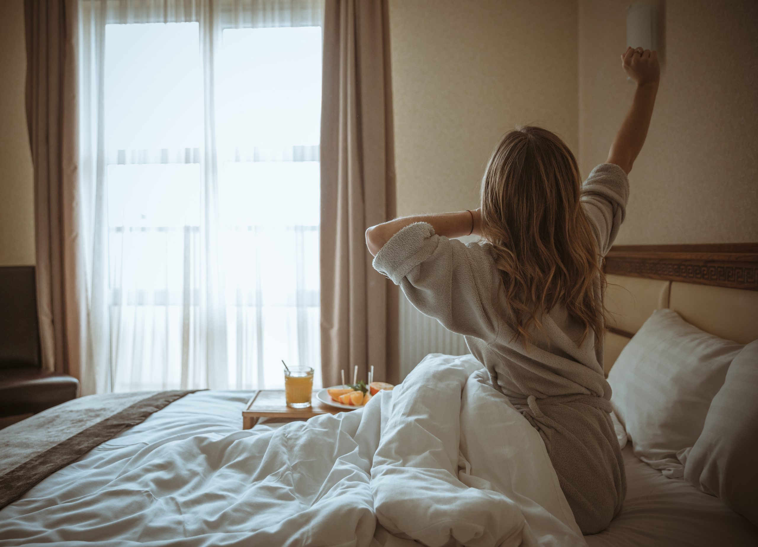 young-woman-sitting-bed-stretching-her-hand-with-breakfast-table